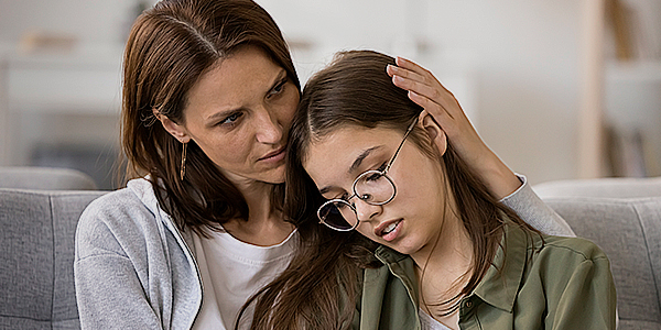 Mãe com a mão na cabeça da filha falando sobre o boletim escolar. 