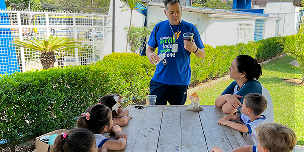 Professor mostra copo aos alunos ensinando práticas sustentáveis do meio ambiente.